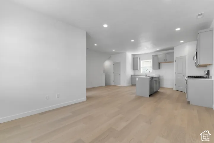 Open-concept interior featuring wood-finish flooring, recessed lighting, and a kitchen equipped with cabinetry, an island, and stainless steel appliances