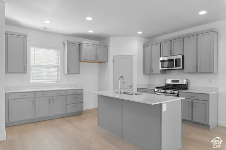 Kitchen featuring shaker-style cabinetry, a central island with a stainless steel sink, stone-finish countertops, wood-finish flooring, and integrated stainless steel appliances