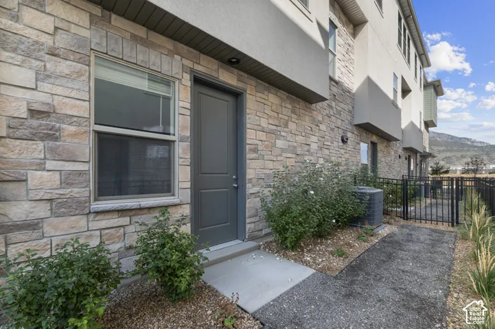 Multi-story exterior featuring stacked stone veneer, metal railings, concrete entryway, and mountain backdrop