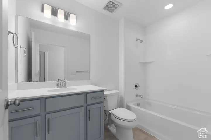 Bathroom featuring a grey vanity with a white countertop, large wall-mounted mirror, polished chrome plumbing fixtures, and a white tile tub surround