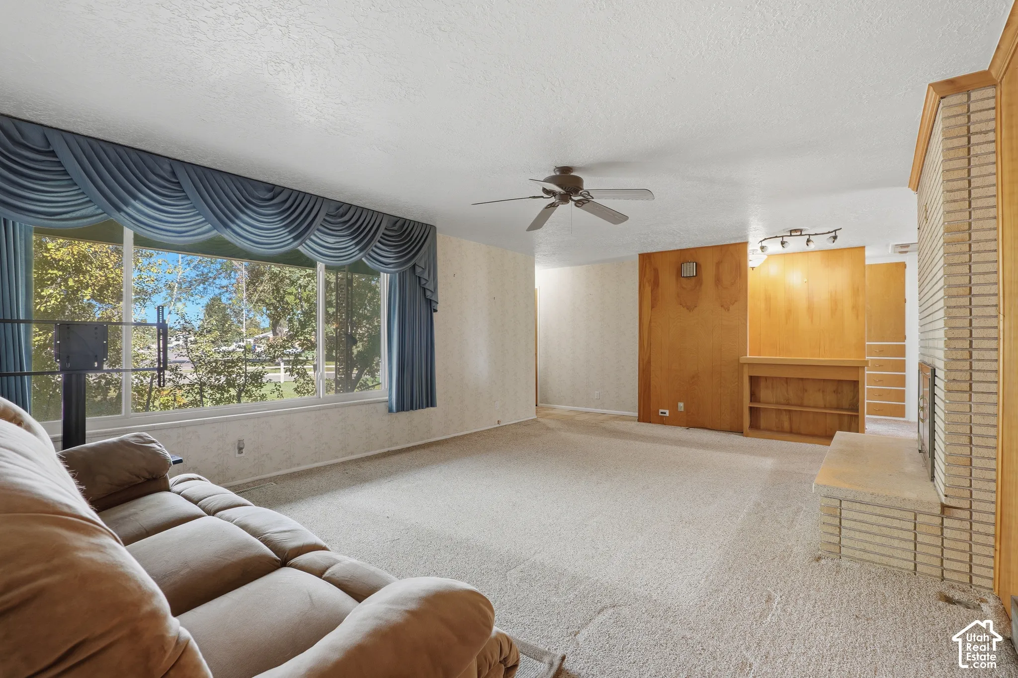 Living area featuring a floor-to-ceiling brick fireplace with a raised hearth, wood paneling, built-in shelving, and a large picture window