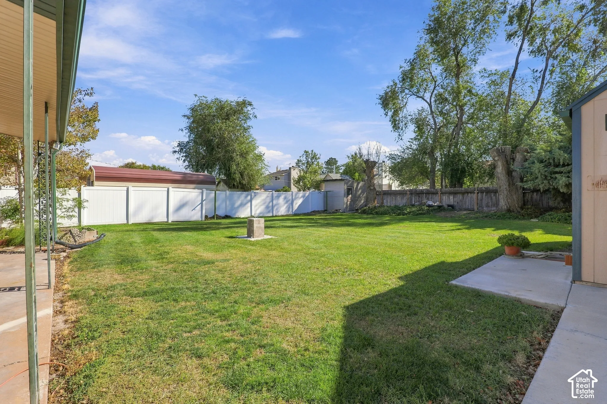 Backyard featuring a grass lawn, white vinyl fencing, concrete patio area, and an external storage structure