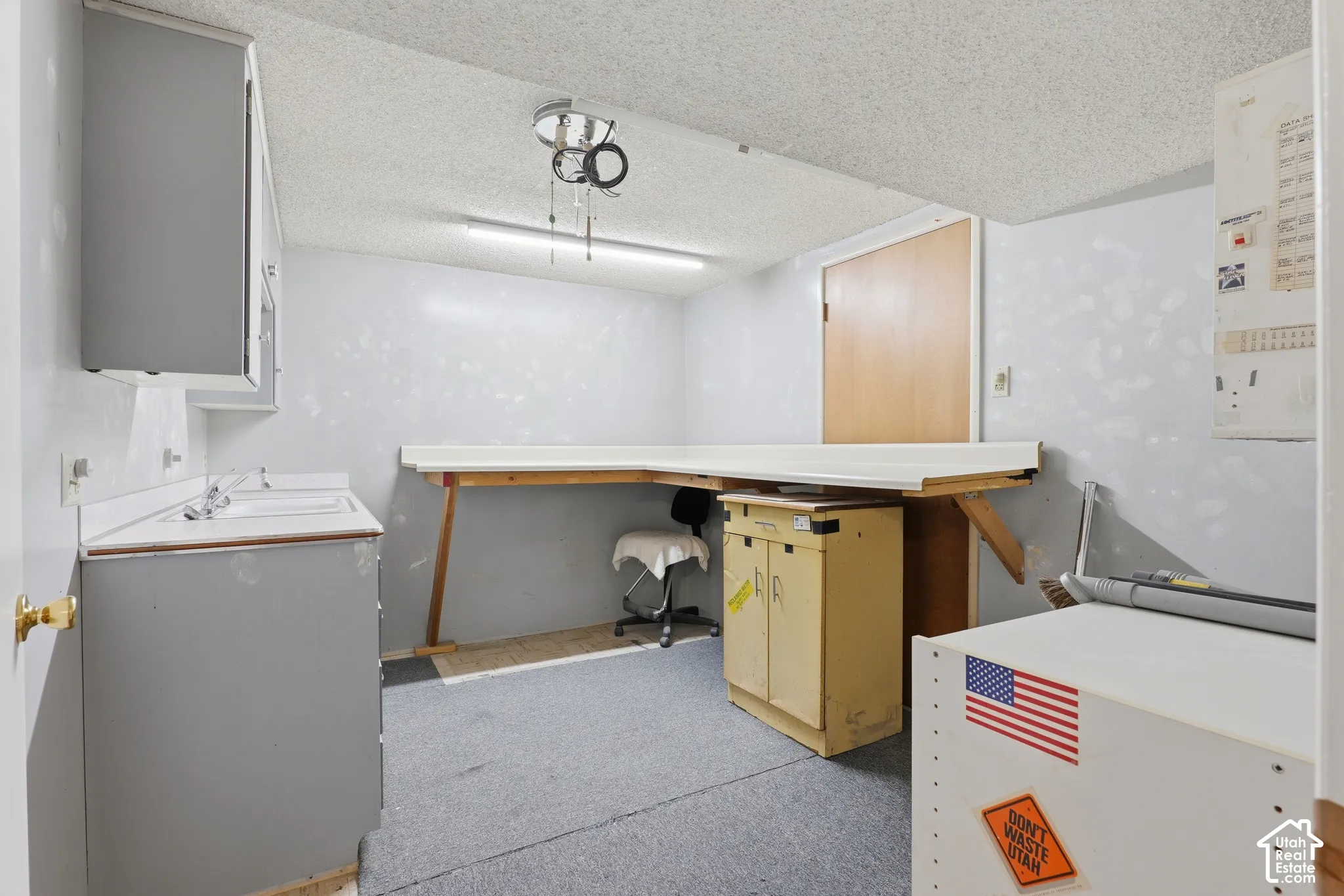 Utility area featuring grey cabinetry, a drop-in sink with a metal faucet, a built-in L-shaped countertop, and overhead fluorescent lighting