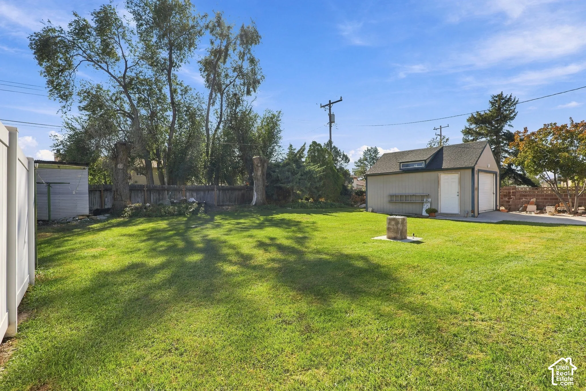 Expansive backyard featuring a grass lawn, detached garage, wood-style fencing, and mature trees