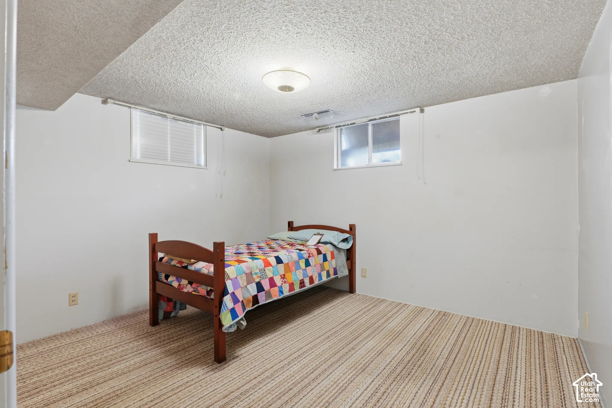 Room featuring neutral-toned carpeting, textured ceiling, dual sliding windows with blinds, and a flush-mount circular ceiling light