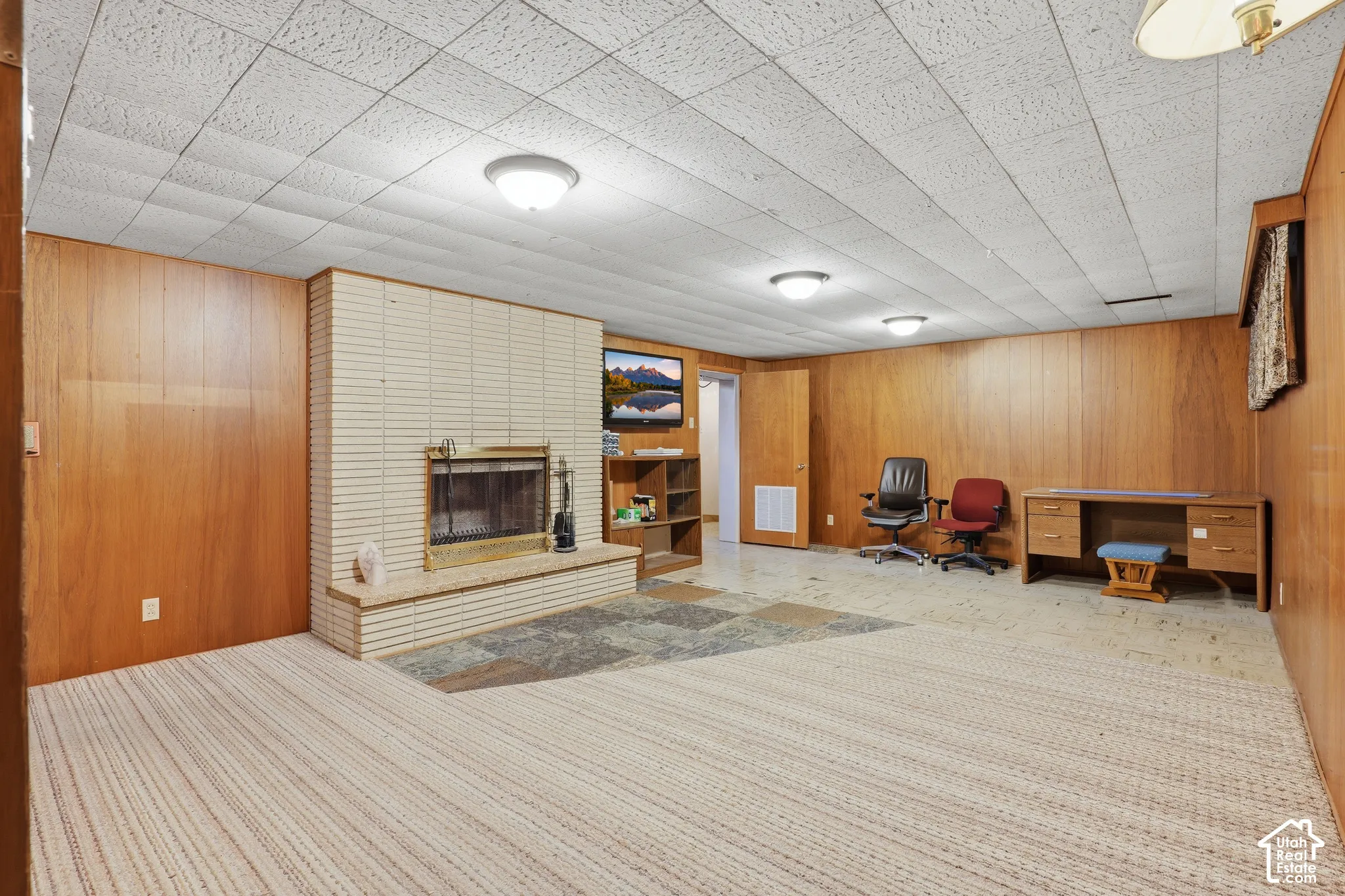 Wood-paneled walls, brick fireplace surround with a raised hearth, stone-tiled floor inlay, and flush-mount lighting fixtures