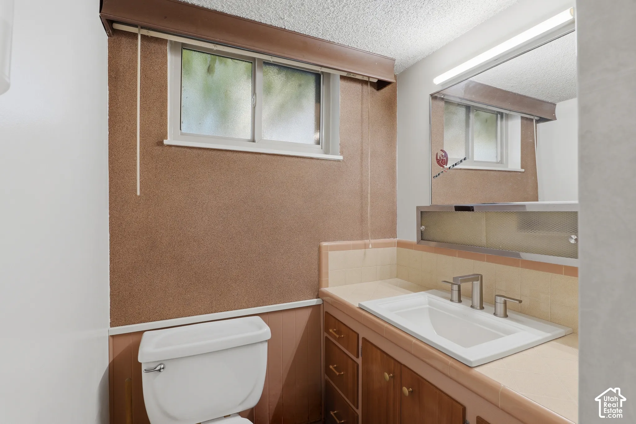 Bathroom vanity featuring a rectangular integrated sink, neutral-tone tile countertop, wood-finish cabinetry, and a mirrored medicine cabinet