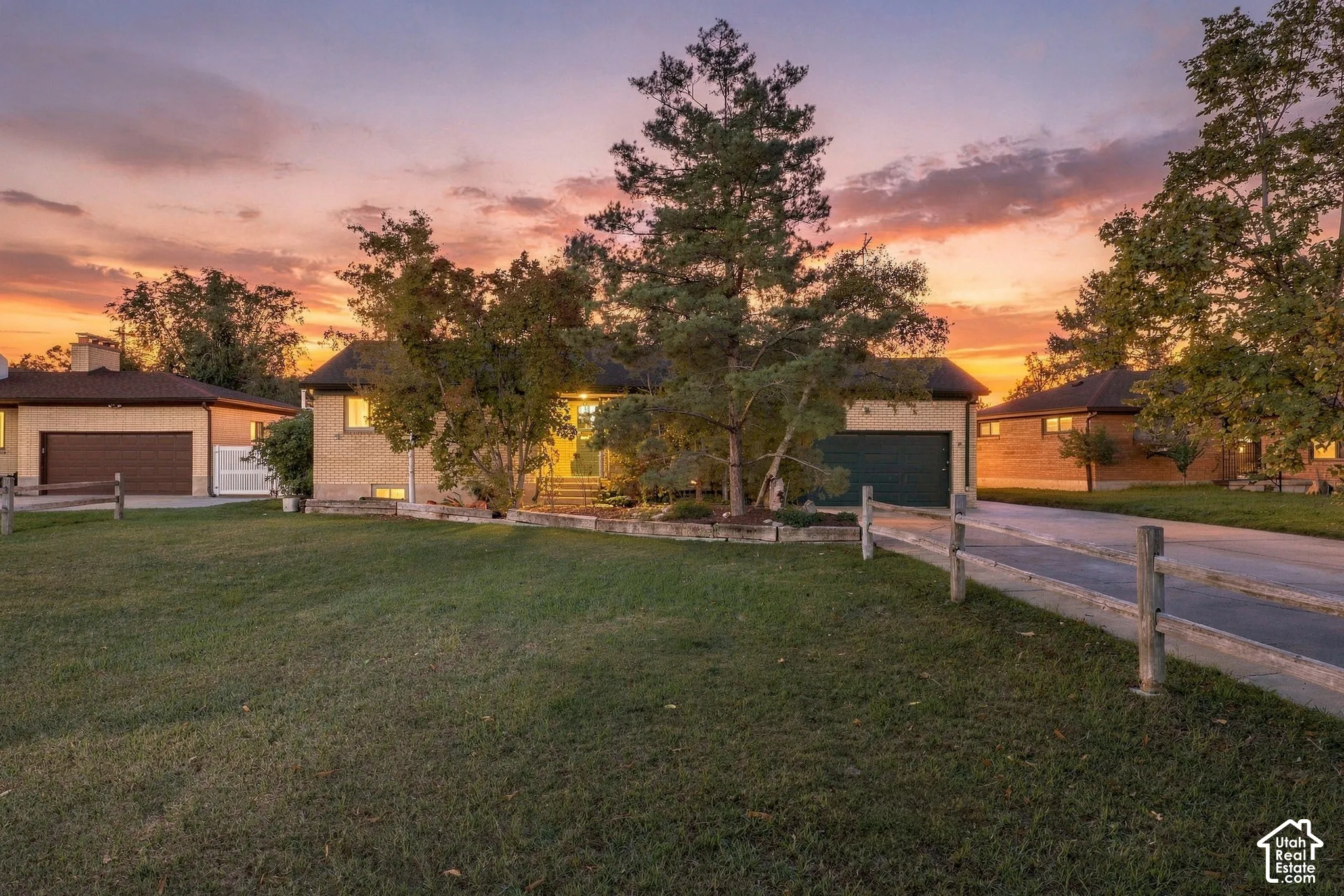 Rambler-style exterior featuring a brick facade, multi-car garage, split-rail fencing, and mature landscaping