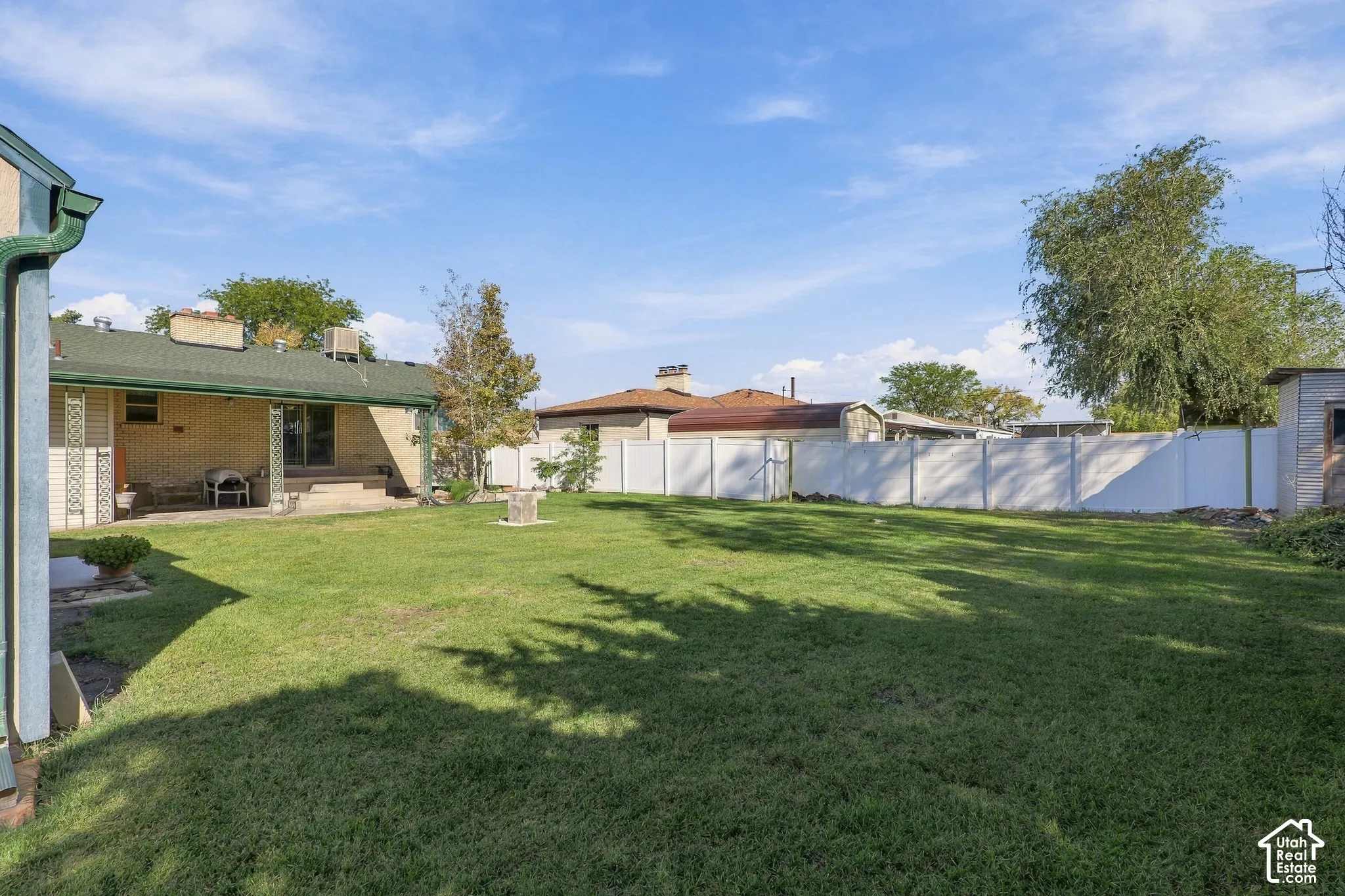 Expansive backyard featuring a large grass lawn, a covered concrete patio, and white vinyl perimeter fencing