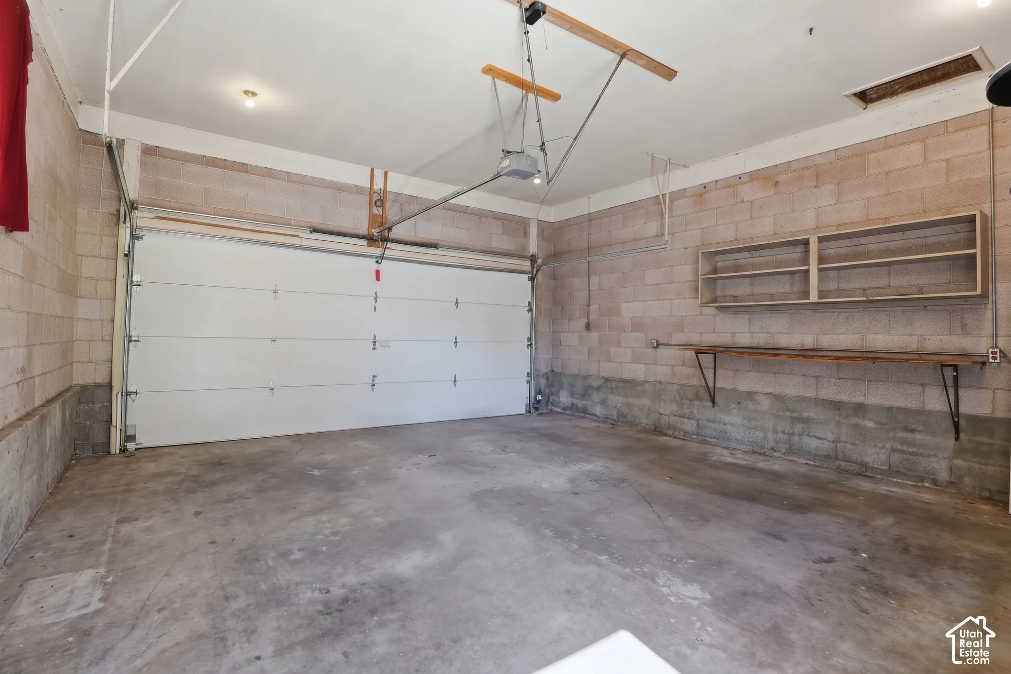 Garage interior featuring exposed concrete masonry unit walls, a white overhead door, concrete flooring, built-in wall shelving, and an attached workbench