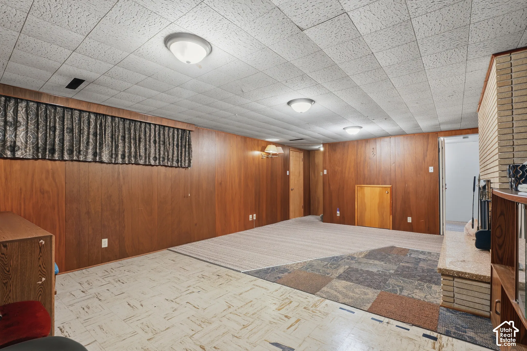 Wood-paneled walls, ceiling-mounted lighting, masonry fireplace surround, and mixed flooring materials