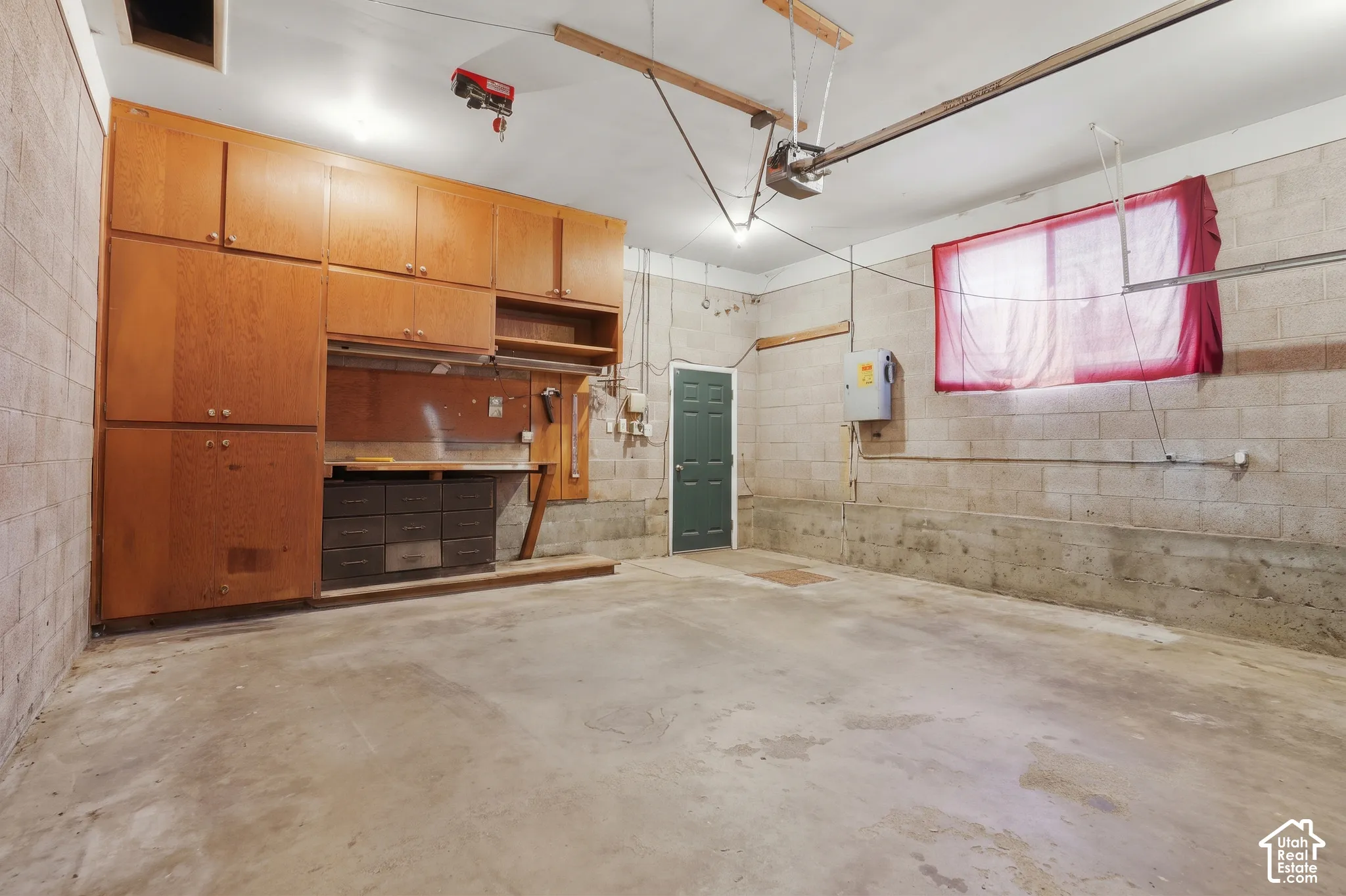 Garage space featuring concrete block walls, built-in wooden cabinetry, a fixed workbench, and an automatic garage door opener