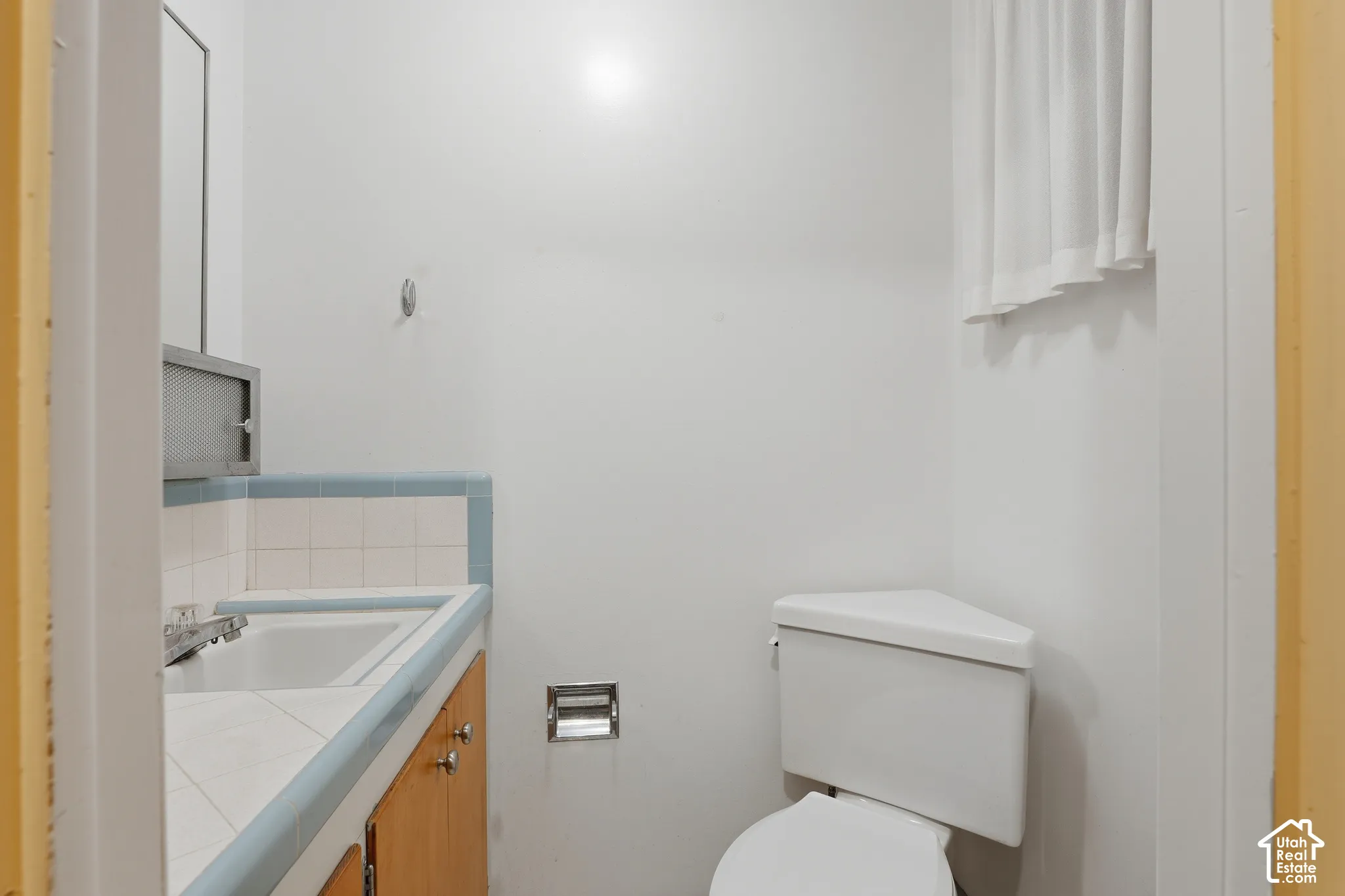 Bathroom featuring a vanity with tile countertop, blue tile backsplash, wooden cabinetry, and corner-mounted toilet