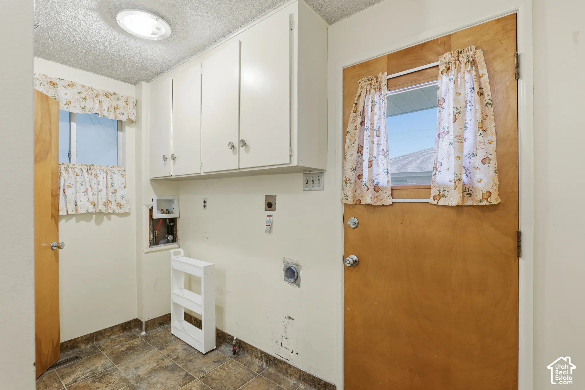Utility area featuring wall-mounted white cabinetry, tile flooring, and a natural wood door with a glass pane