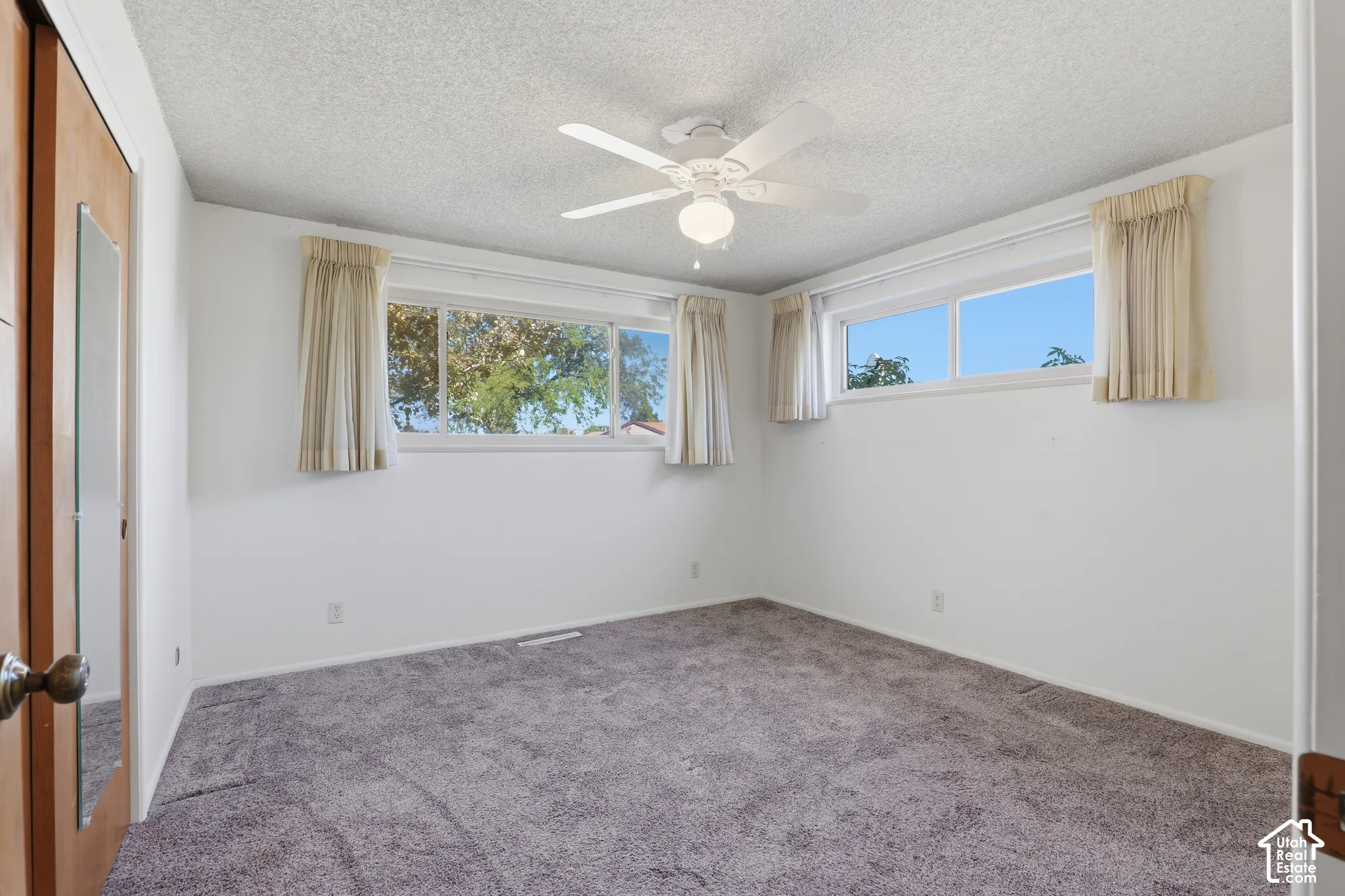Room featuring neutral carpeting, a ceiling fan with integrated lighting, dual horizontal windows, and a closet with a full-length mirrored door