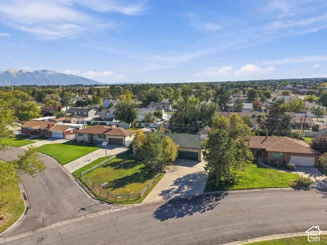 Aerial perspective of a single-story residence on a corner lot featuring an attached garage, a fenced front yard, and a mountain range backdrop