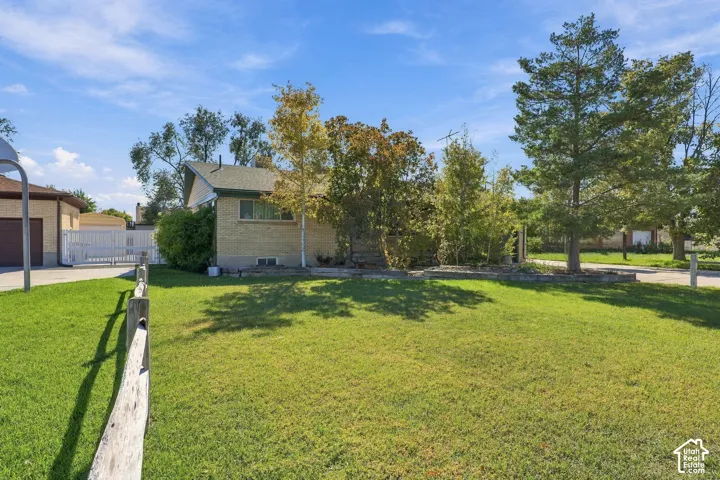 Brick exterior residence featuring a sprawling lawn, mature trees, and a wooden perimeter fence