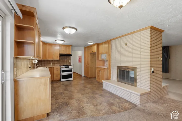 Kitchen featuring custom wood cabinetry, tiled backsplash, built-in range, and a dual-sided brick fireplace with a raised hearth