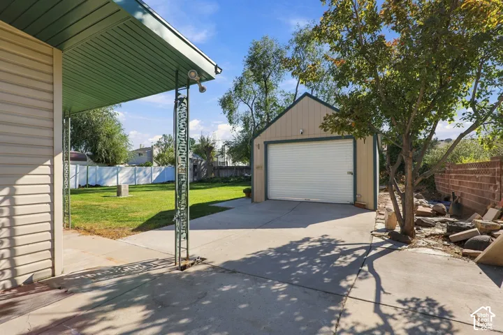 Detached garage with a concrete driveway, covered patio, manicured lawn, and brick perimeter wall