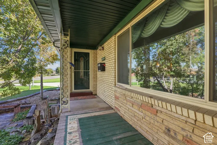 Exterior entrance featuring light-colored brick siding, decorative metal porch pillar, large picture window, and covered porch with painted decking