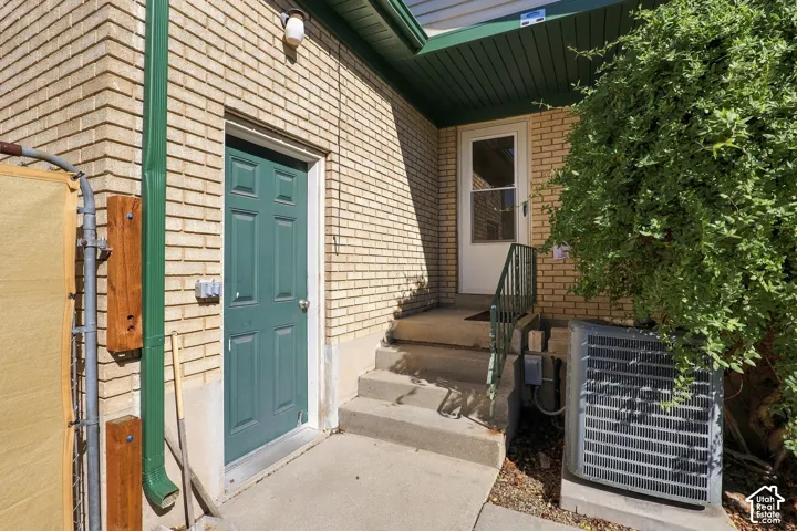 Exterior featuring tan brick masonry, solid panel green entry door, concrete steps, metal handrail, and green painted fascia trim