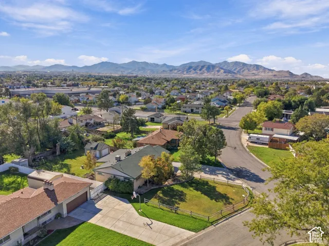 Aerial perspective of a suburban neighborhood featuring a corner lot with a fenced lawn, concrete driveway, and expansive mountain scenery