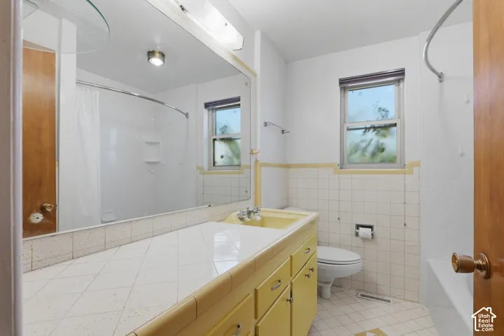 Bathroom featuring a built-in vanity with an integrated sink, expansive wall-mounted mirror, diamond-patterned tiled countertop, and a shower-tub combination with surrounding tile finish