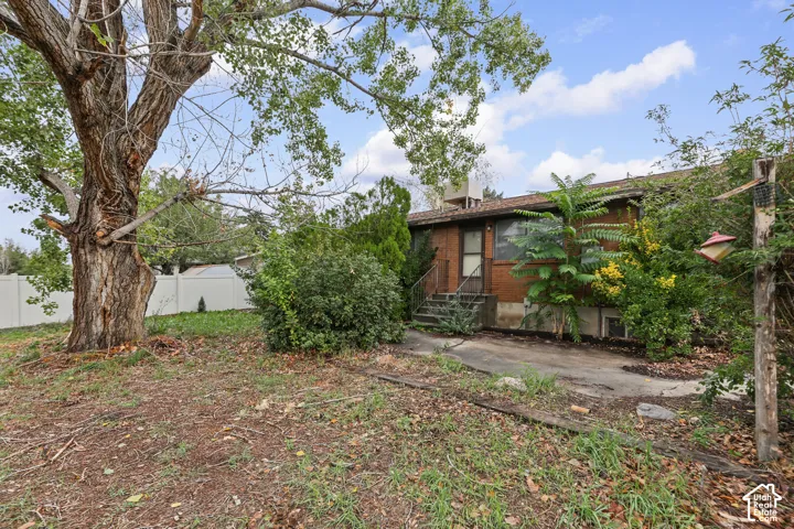 Brick exterior facade featuring a concrete patio, mature trees, and vinyl privacy fencing