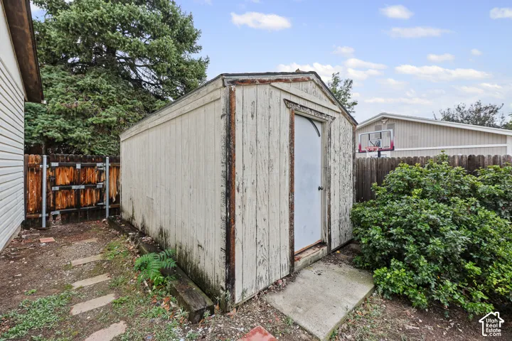 Detached exterior storage structure featuring wood-panel siding, a gabled roof, and a concrete paver entrance