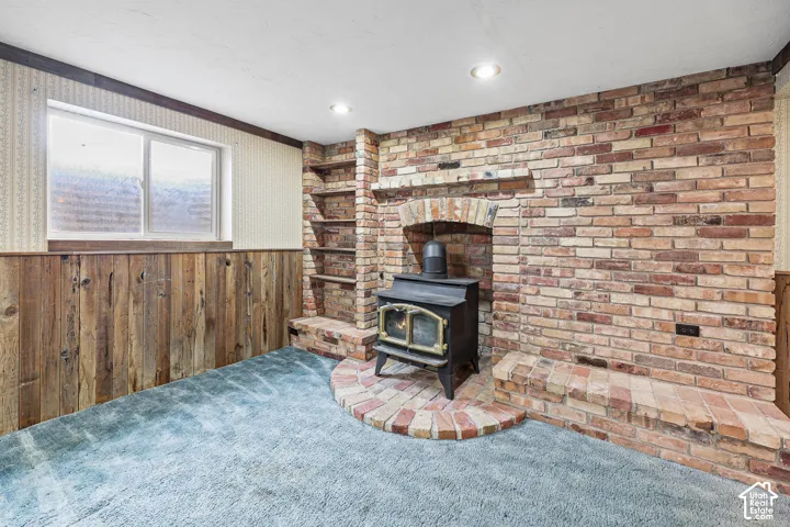 Floor-to-ceiling brick fireplace surround with a raised brick hearth, integrated brick shelving, wood-burning stove, and vertical wood panel wainscoting