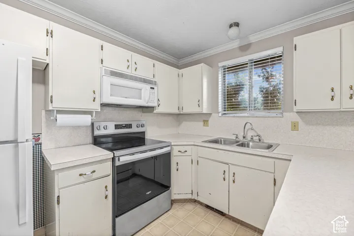 Kitchen featuring white cabinetry, solid-surface countertops, dual-basin stainless steel sink, over-the-range microwave, and tile flooring