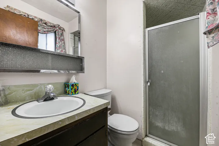 Ensuite Bathroom featuring a vanity with an integrated oval sink, countertop with a marbled finish, chrome-trimmed wall mirror, and a walk-in shower with a framed glass door