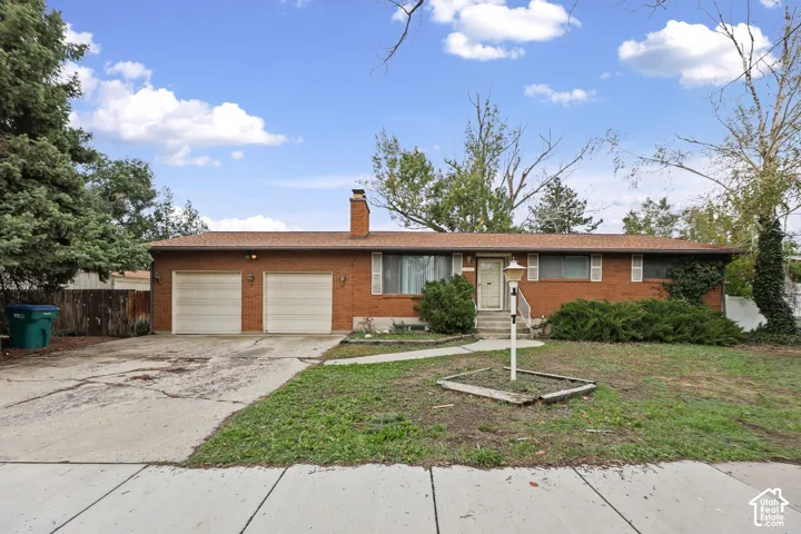 Single-level brick exterior featuring a multi-car attached garage, central masonry chimney, and concrete driveway