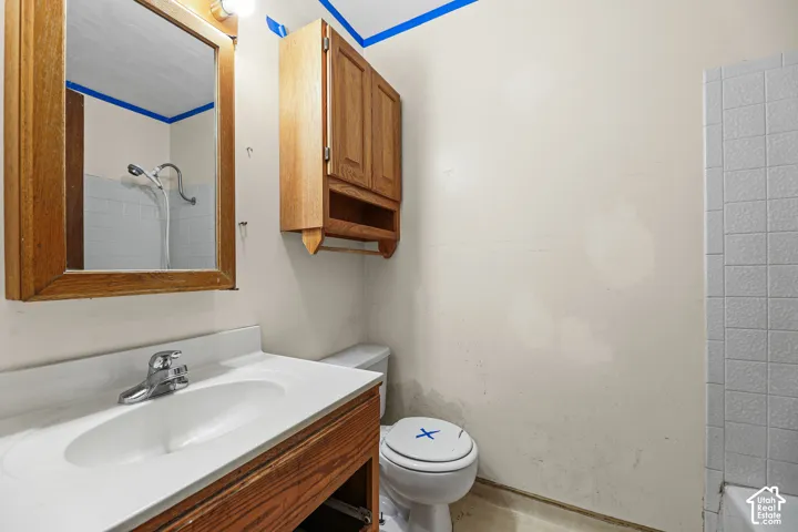 Bathroom featuring a wood-finish vanity with an integrated basin, wall-mounted wood-finish cabinetry, a rectangular wall-mounted mirror, and a tiled shower surround