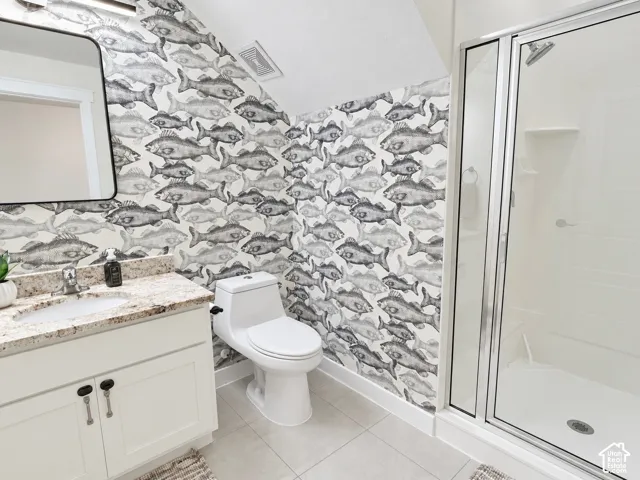 Bathroom featuring a custom vanity with stone-finish countertop, undermount sink, porcelain tile flooring, and a glass-enclosed shower