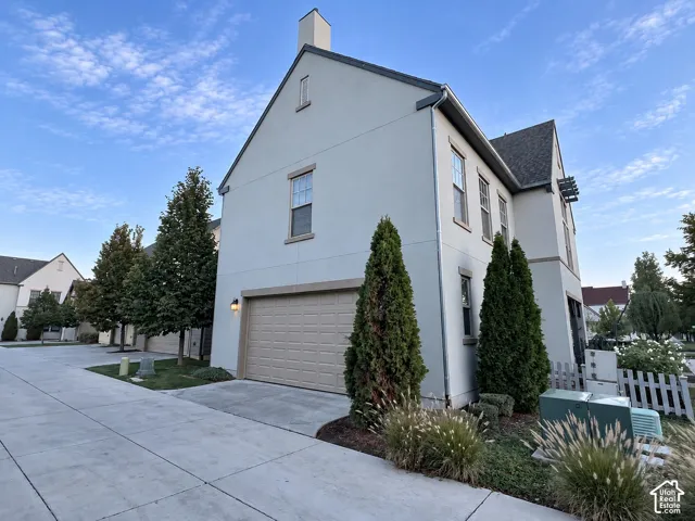 Stucco exterior with a peaked roofline, attached multi-car garage, and professionally landscaped shrubbery