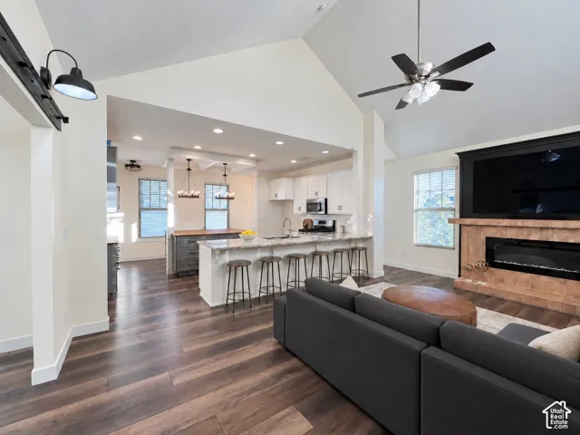Vaulted ceiling living area featuring a fireplace with stone-finish surround, wood-finish flooring, recessed lighting, and a kitchen with white cabinetry and a stone-topped peninsula