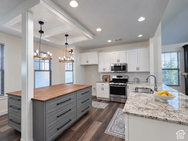 Kitchen featuring a central island with a wood countertop, perimeter cabinetry with stone-finish surfaces, stainless steel appliances, wood-finish flooring, and a coffered ceiling element with pendant lighting