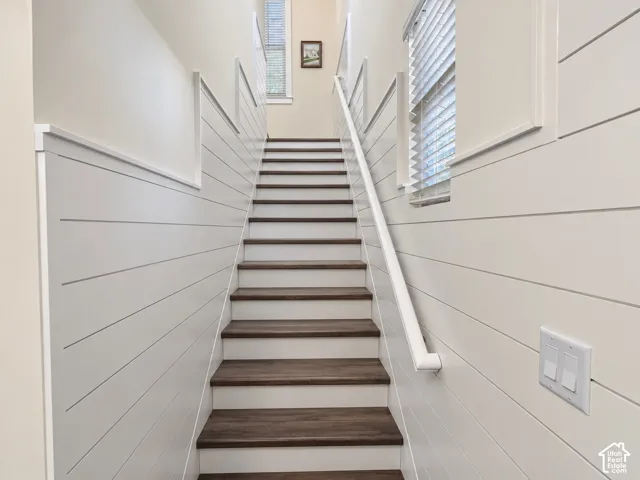 Staircase featuring horizontal shiplap wall paneling, wood-finish treads, white risers, and a minimalist wall-mounted handrail