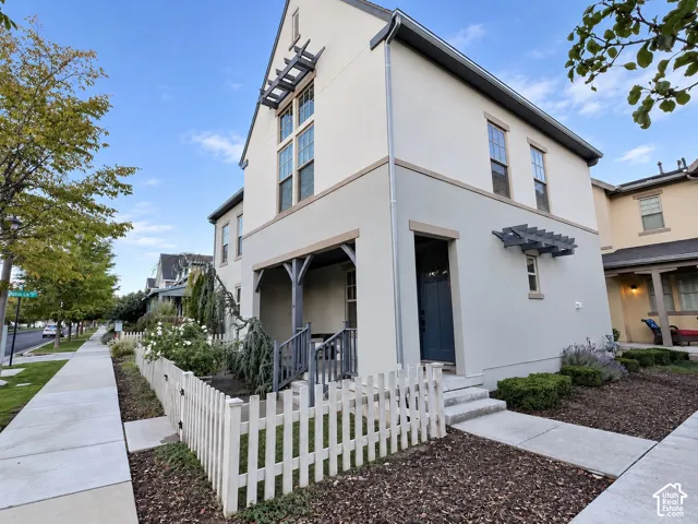 Stucco exterior featuring a covered front porch, decorative pergola elements, multi-pane windows, and a picket fence