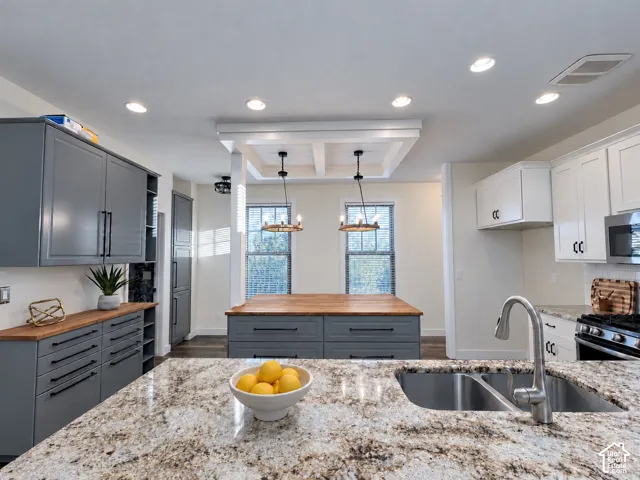 Kitchen featuring charcoal-grey cabinetry, light-toned stone countertops, a dual-basin stainless steel sink with a high-arch faucet, a wood-topped center island, and recessed ceiling lighting