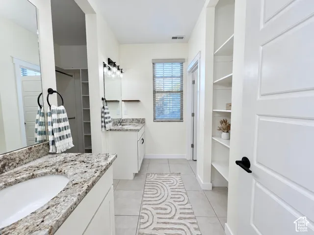 Bathroom featuring a dual-sink vanity with stone countertops, tile flooring, built-in open shelving, and wall-mounted light fixtures