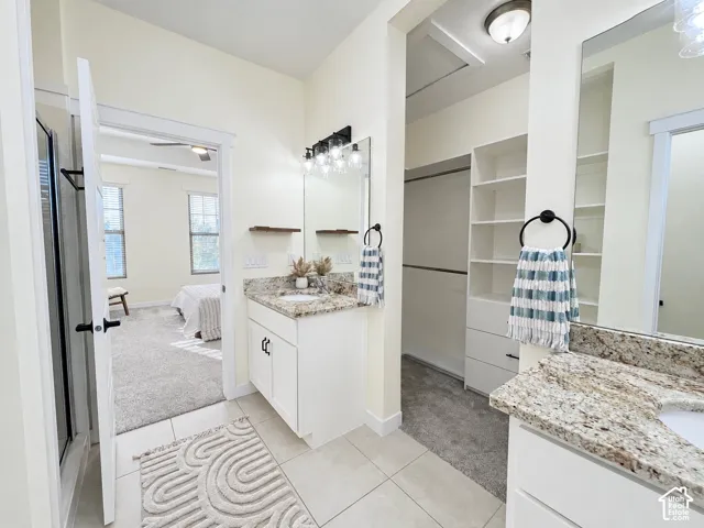 Bathroom featuring dual vanities with stone-finish countertops, undermount sinks, white cabinetry, and built-in closet shelving