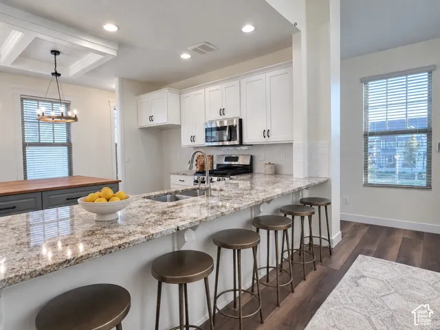 Kitchen featuring white cabinetry, stone-surface countertops, a center island with a wood-finish surface, stainless steel appliances, and wood-finish flooring