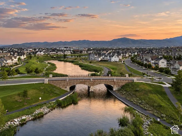 Stone arch bridge over a waterway, paved walking paths, landscaped green space, and mountain backdrop