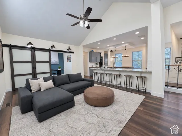 Vaulted ceilings, wood-finish flooring, sliding barn-style doors with frosted glass, quartz-topped island with bar seating, and recessed lighting