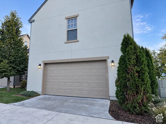 Stucco exterior featuring a two-car garage, recessed panel garage door, single-paneled window with muntins, and dual wall-mounted carriage-style light fixtures