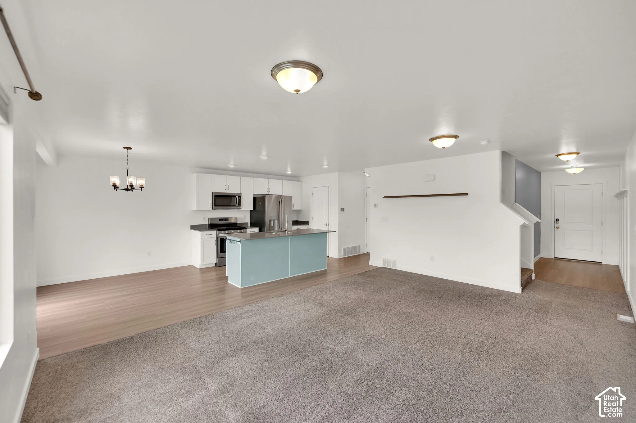 Open-concept kitchen featuring white cabinetry, stainless steel appliances, a center island with a colorful base, wood-finish flooring, and neutral carpeted flooring