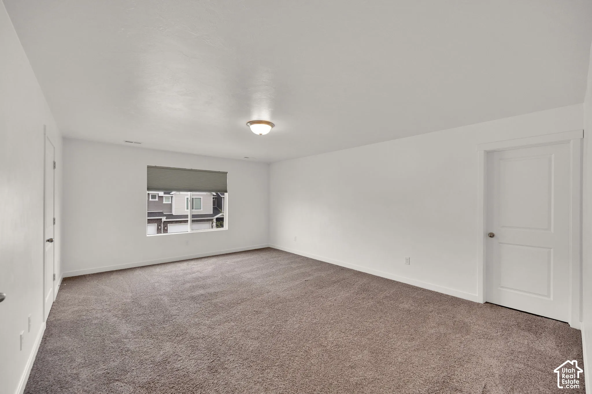 Neutral-toned interior space featuring plush carpeting, smooth wall finishes, a single-light ceiling fixture, and a white two-panel interior door