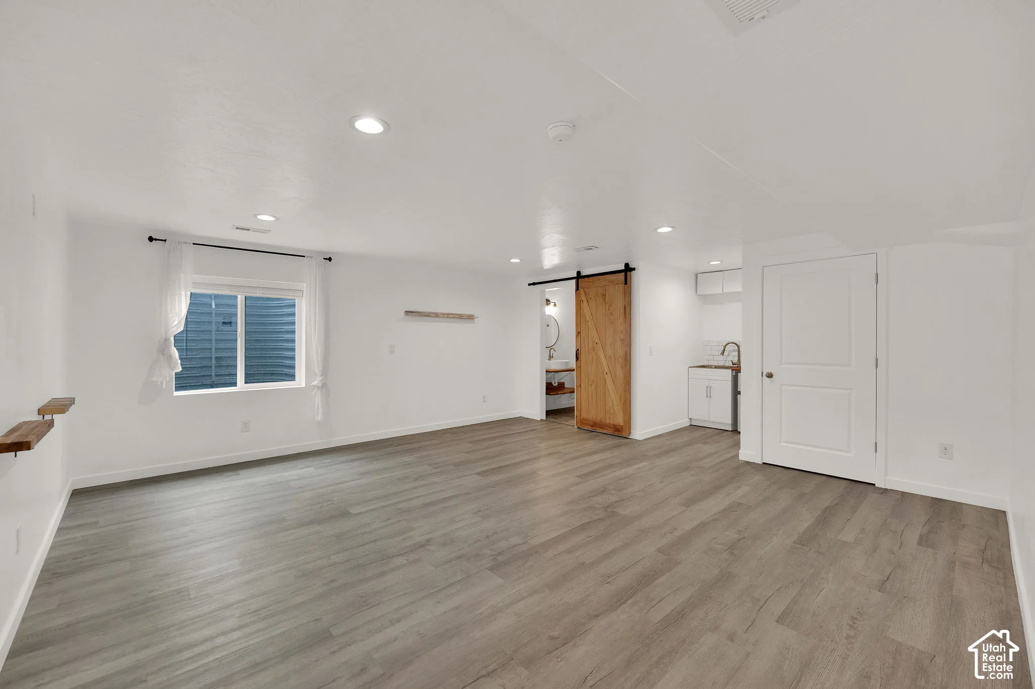 Open-concept room featuring wood-finish flooring, recessed lighting, a sliding barn-style door, and a built-in kitchenette with cabinetry and a sink